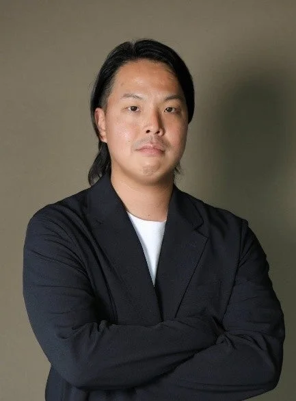 正面を向いて腕を組んだ、黒いジャケットと白いTシャツを着用したアジア人男性のポートレート